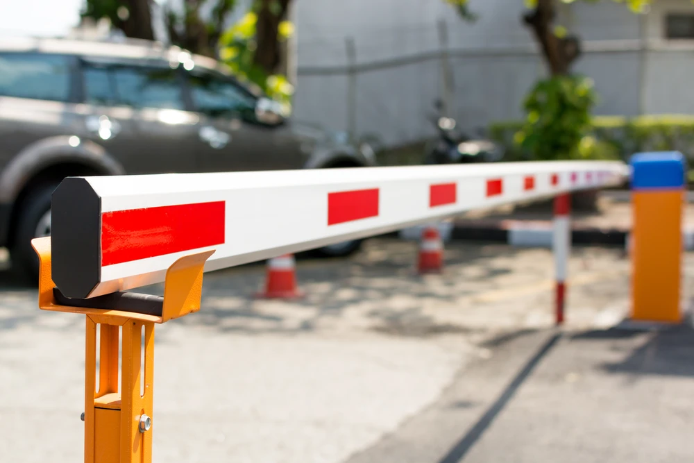Extérieur urbain avec barrière levante automatique orange et blanche à rayures rouges contrôlant l'accès véhiculaire