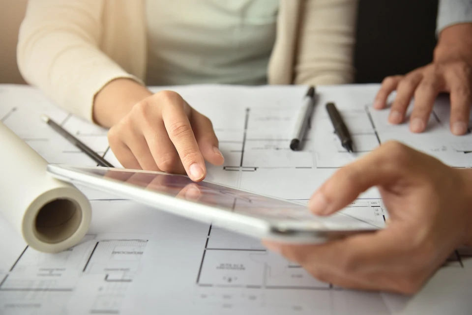 Professionnel en costume consultant des plans architecturaux sur tablette numérique et documents papier