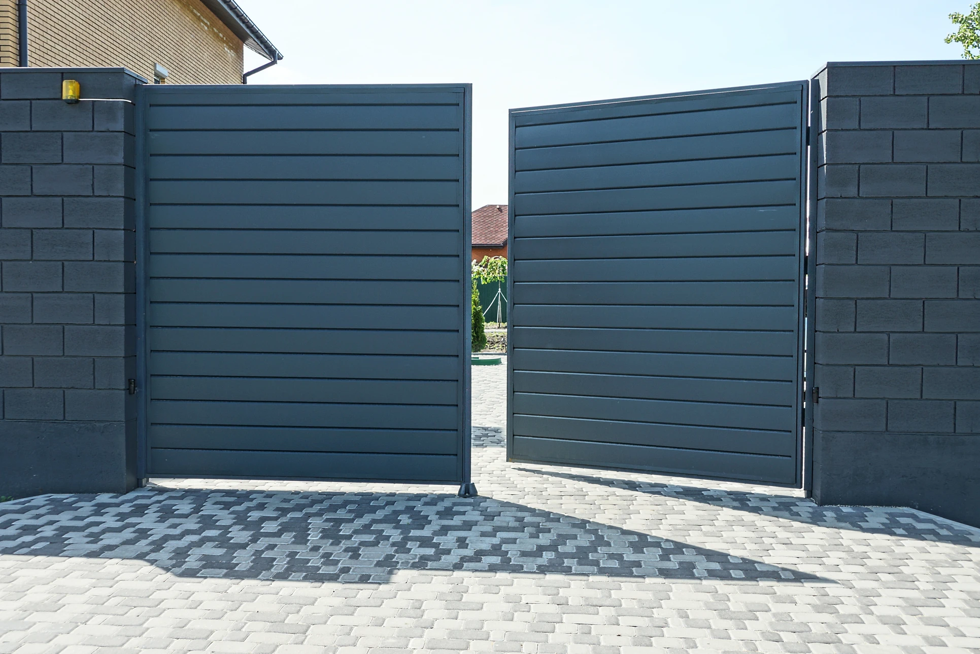 Deux techniciens en combinaison orange et noire installent une porte de garage sectionnelle blanche dans un garage résidentiel