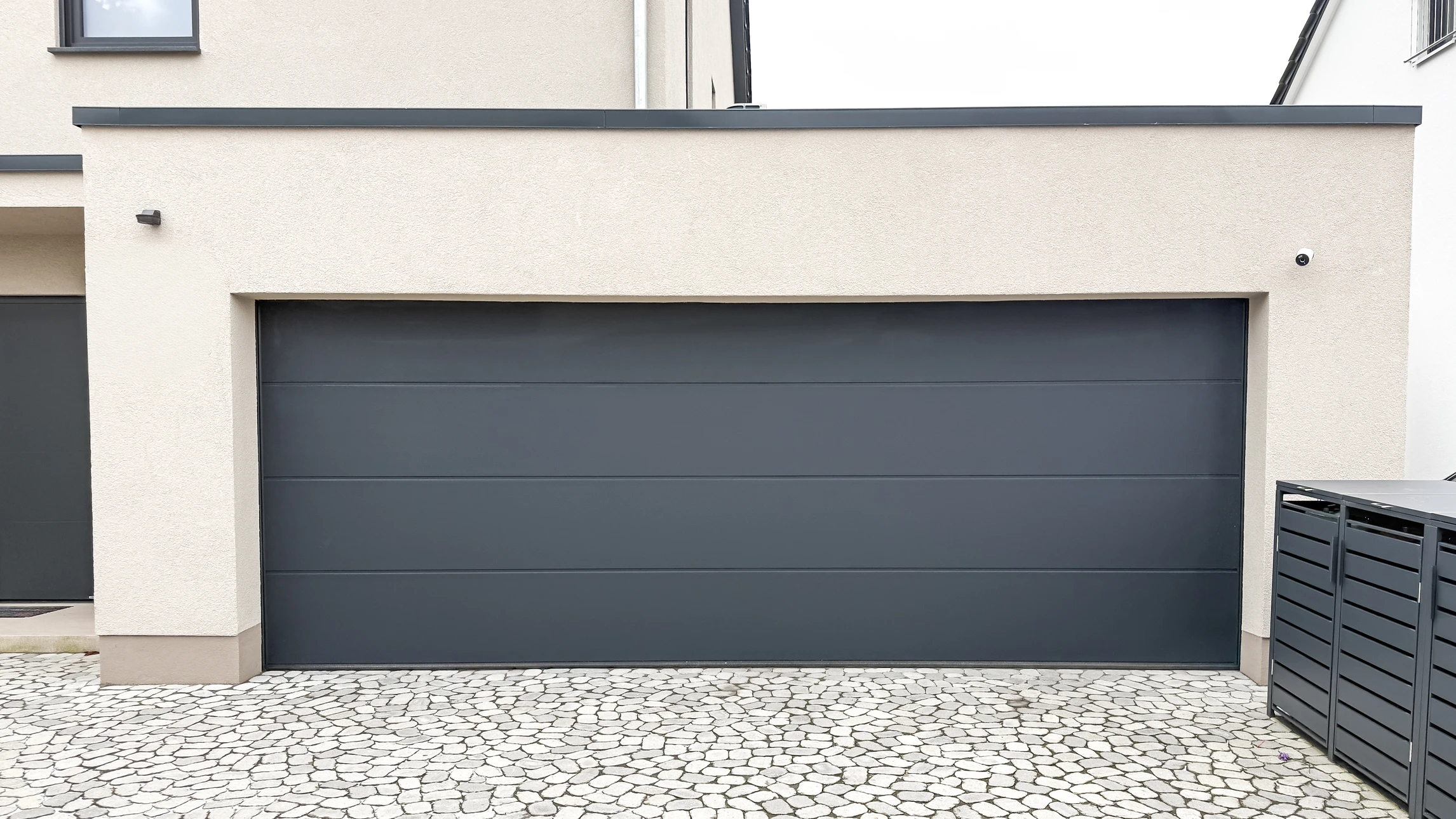 Façade extérieure résidentielle avec porte de garage sectionnelle beige fermée, intégrée dans mur en briques claires